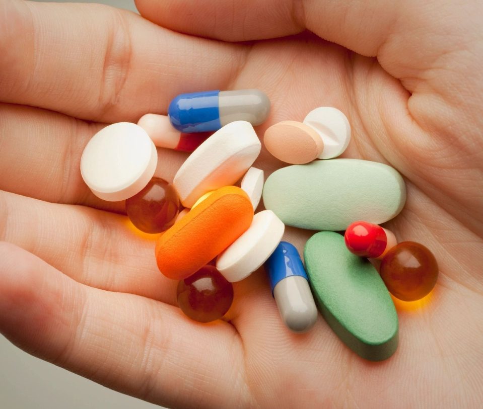 A person holding many different pills in their hand.