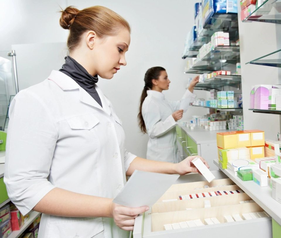 Two women in lab coats are working at a pharmacy.