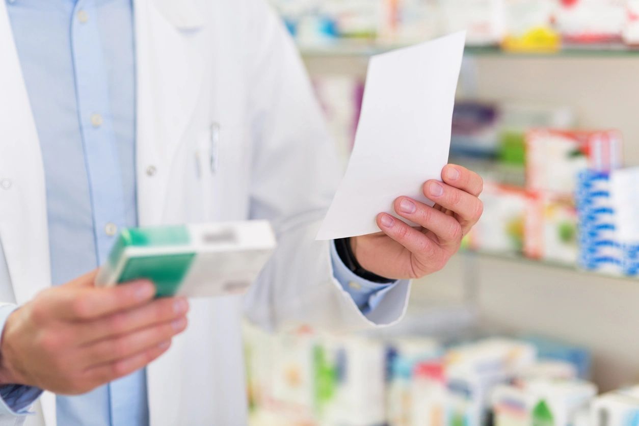 A pharmacist holding a package of medicine and papers.